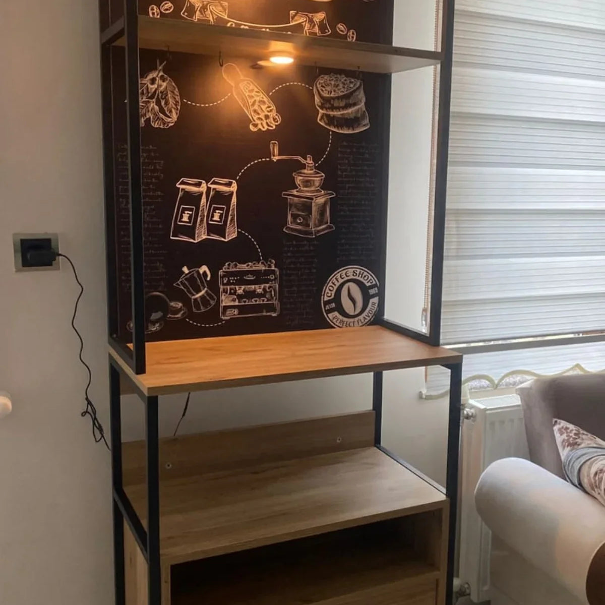 Wooden coffee-themed display cabinet with a light on, placed in a room with a sofa and window blinds.