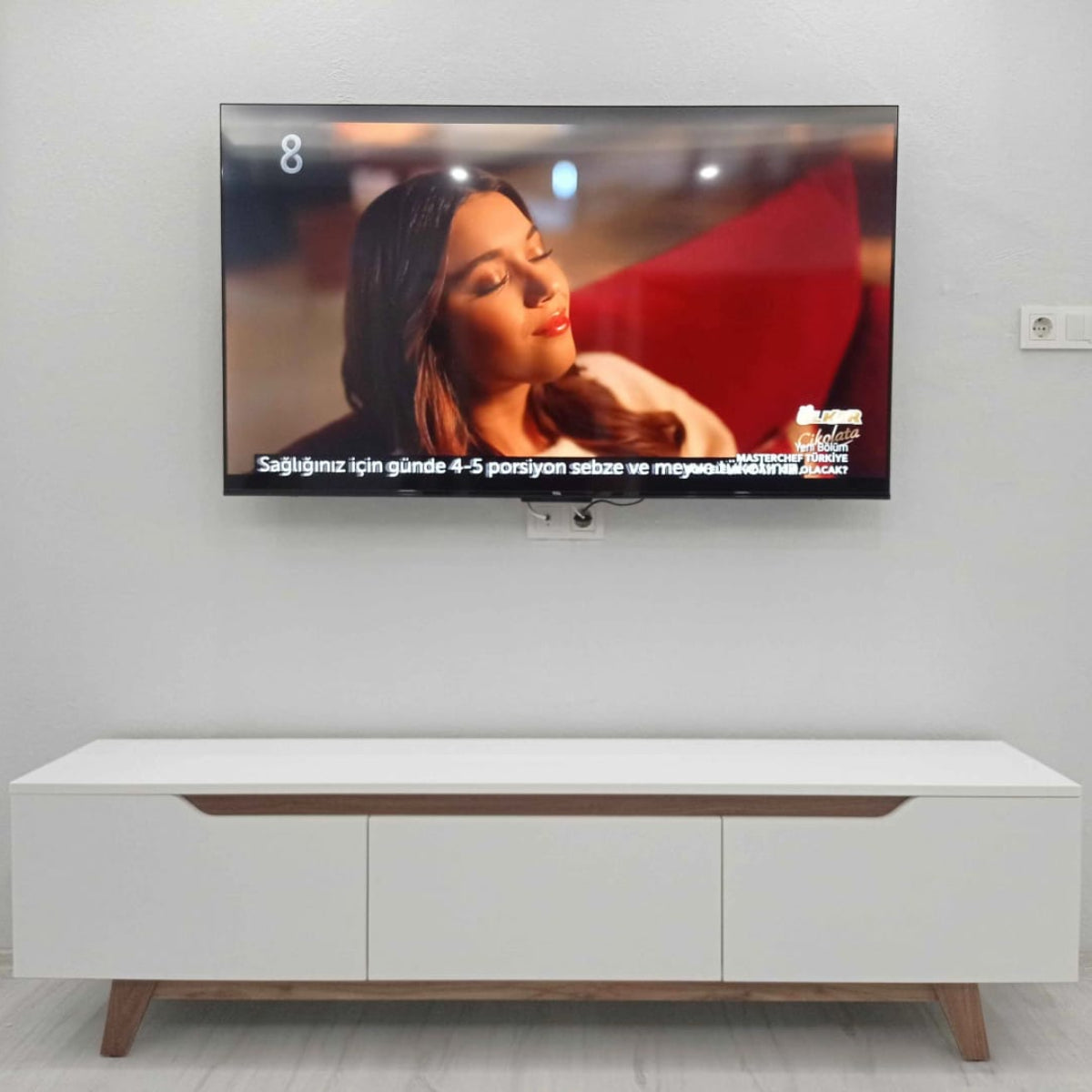 TV mounted on a wall with a white cabinet below