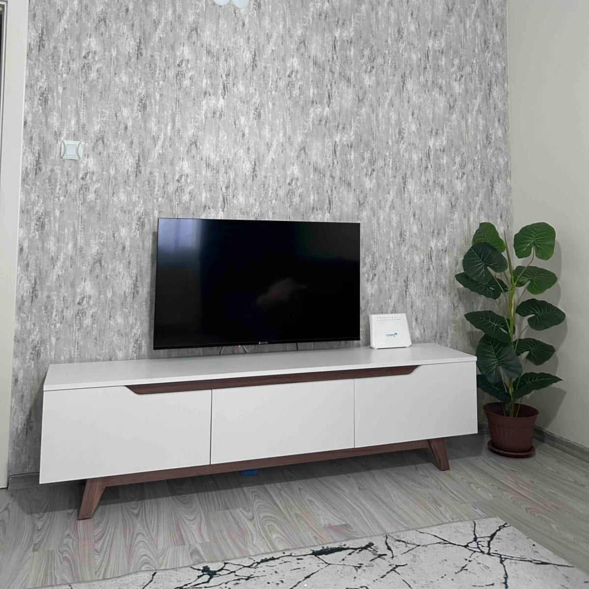 Modern living room with a TV on a white entertainment console against a gray textured wall.