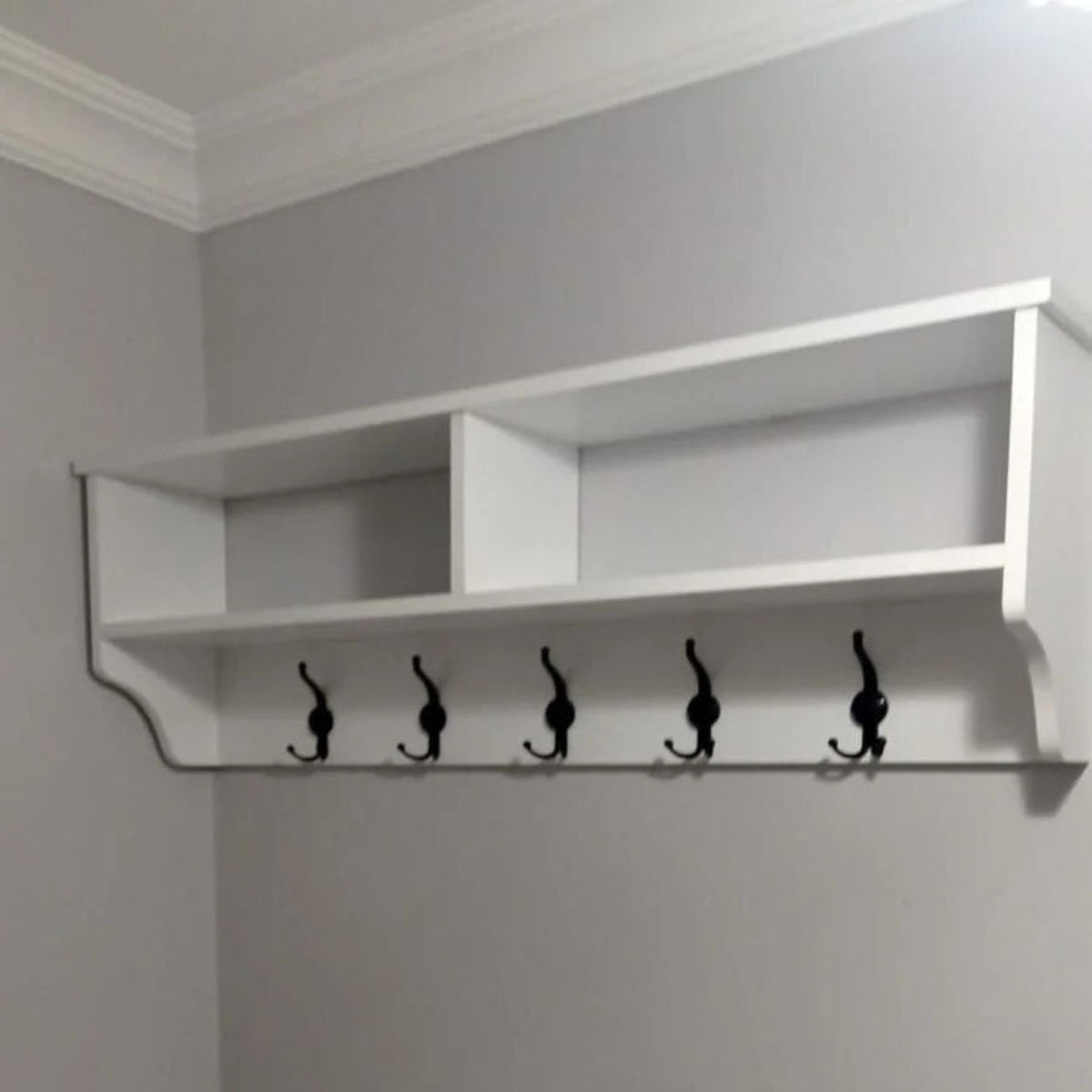 White wall-mounted shelf with hooks against a gray wall