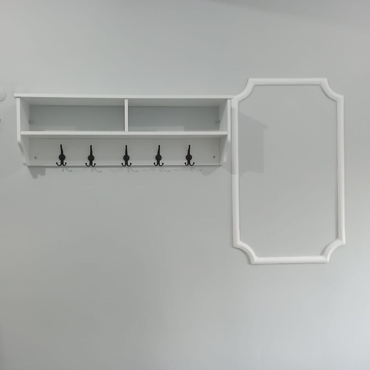 White wall-mounted shelf with hooks on a gray wall.