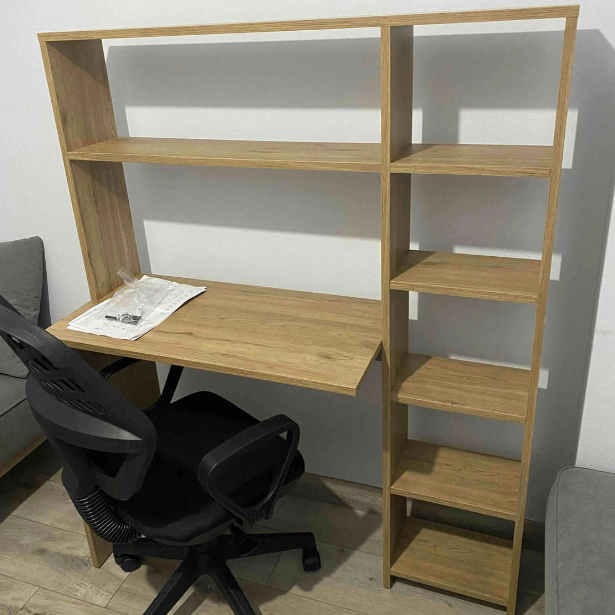 Wooden study desk with shelves and a black office chair in a room.