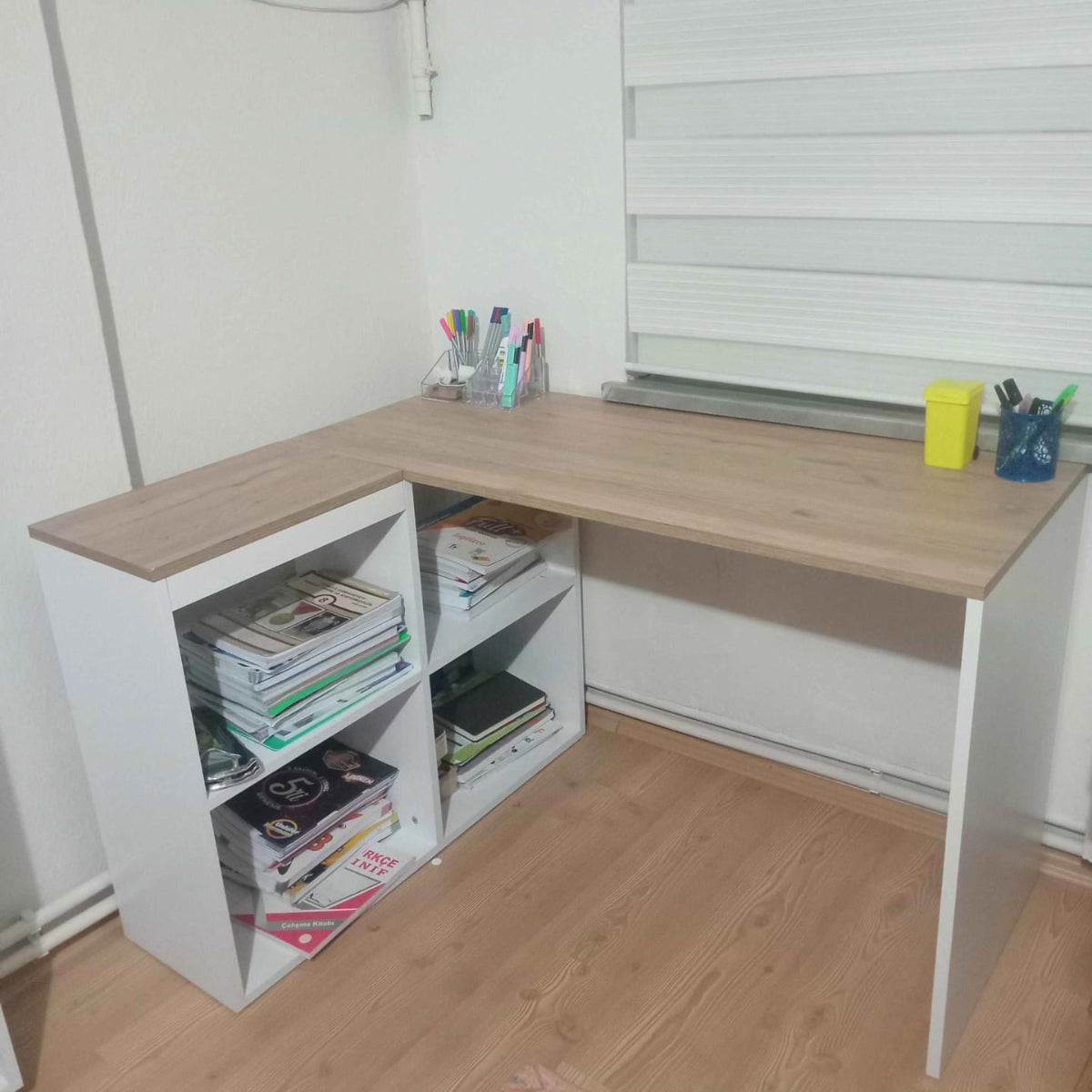 Corner desk with wooden top and white sides, filled with books and stationery items.