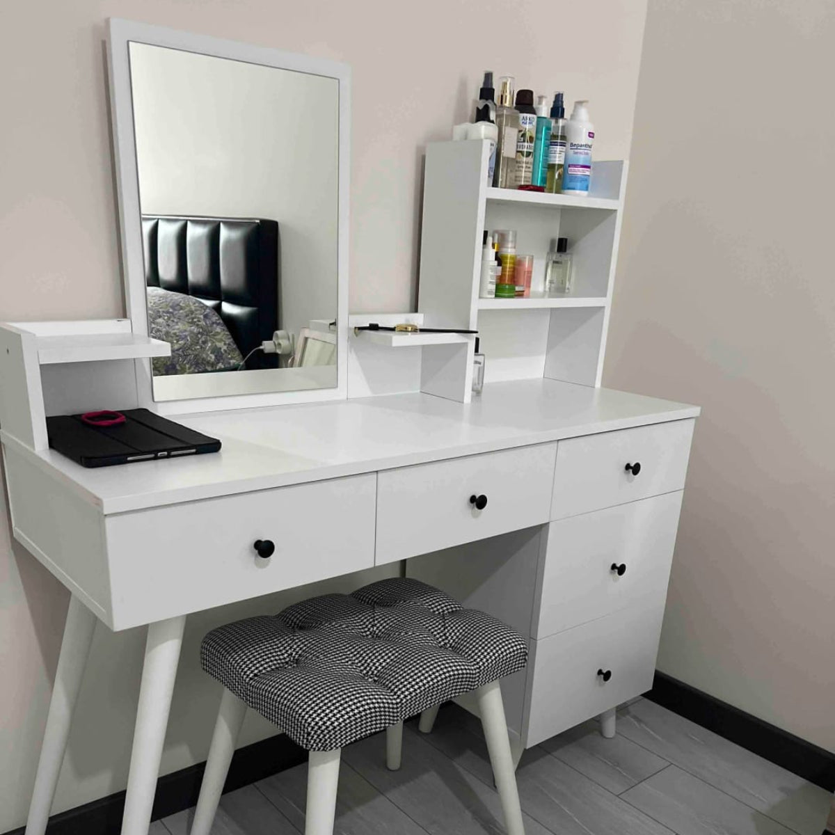White vanity table with mirror, drawers, and stool in a room setting.