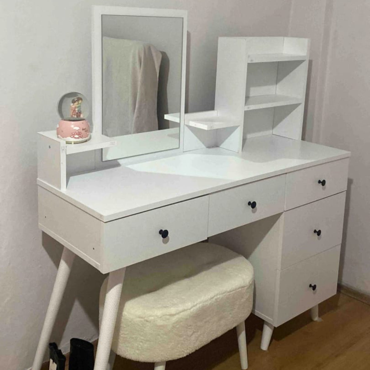 White vanity table with mirror and stool against a plain wall.
