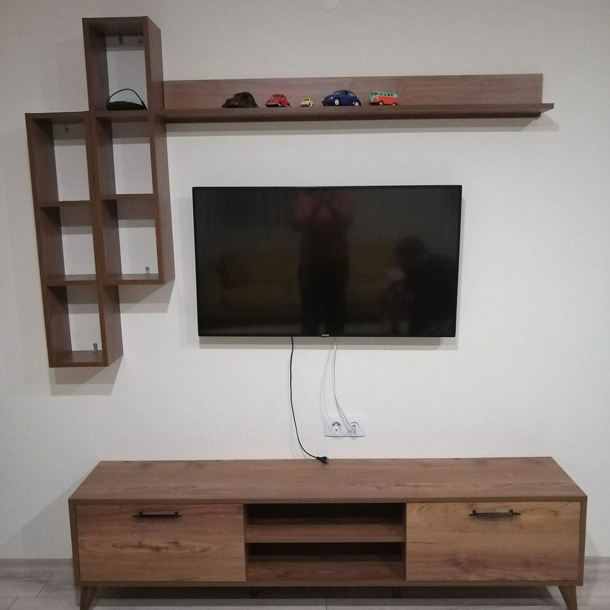 Wooden entertainment unit with shelves and a TV against a white wall.