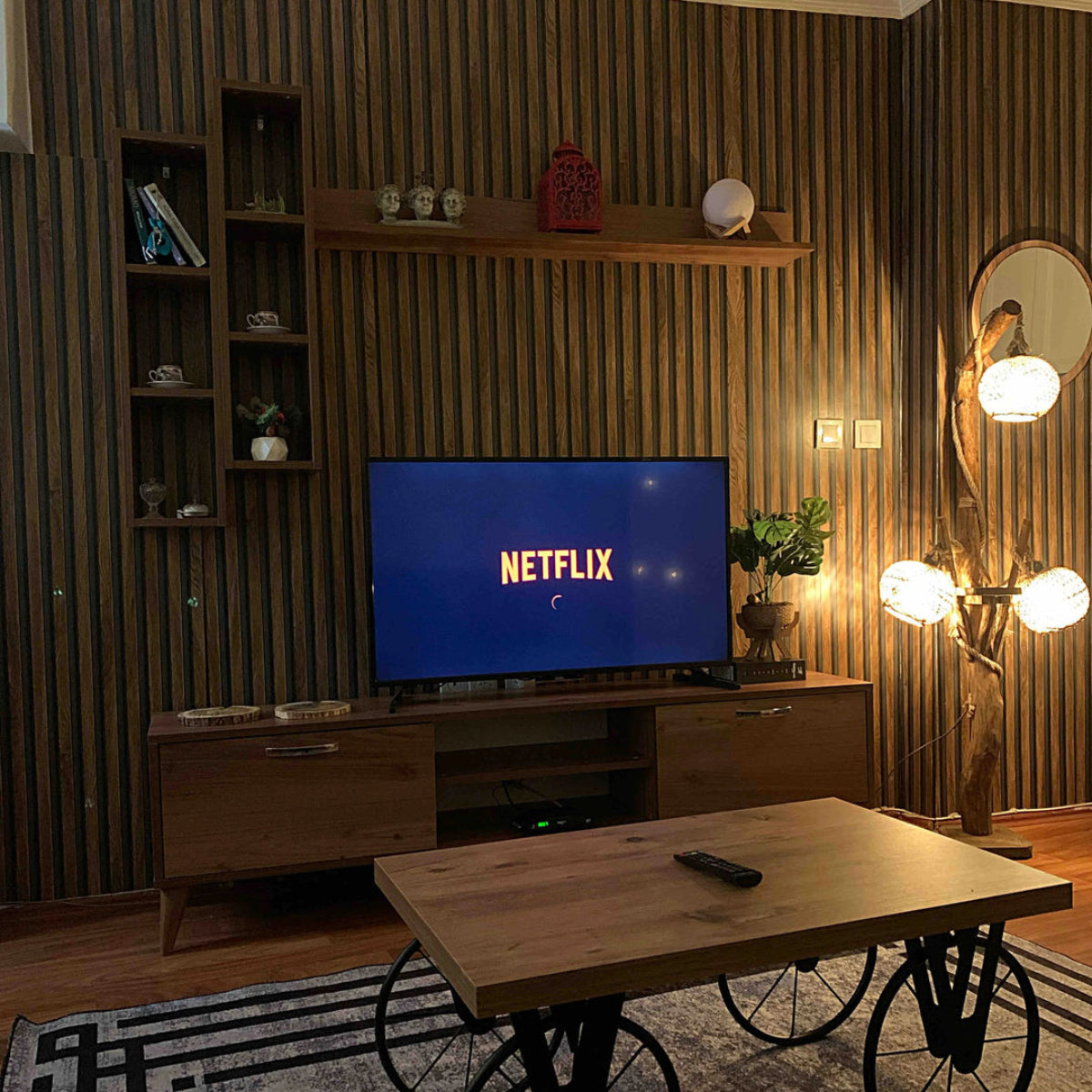 Living room with a TV displaying the Netflix logo, wooden coffee table with wheels, and decorative wall shelves.