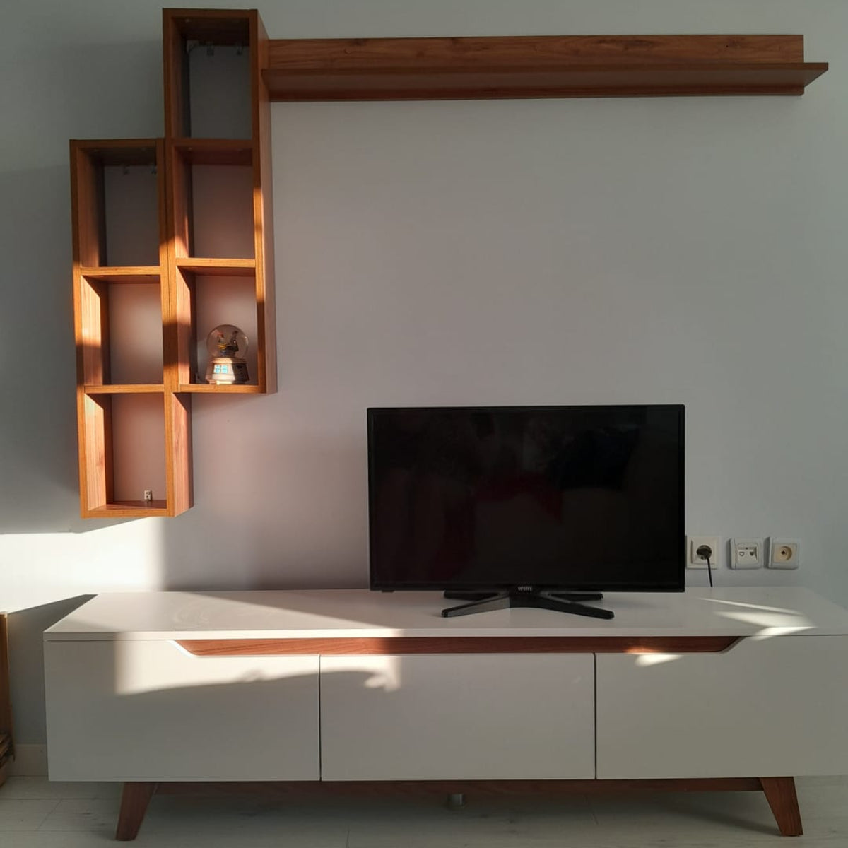Modern living room with a white entertainment console, wooden shelves, and a TV.
