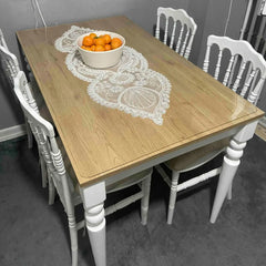 Wooden dining table with white chairs and a bowl of oranges on a gray floor.