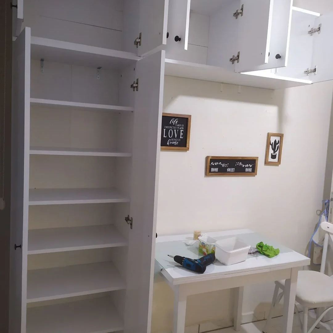 White kitchen with open cabinets revealing a small table and chairs.