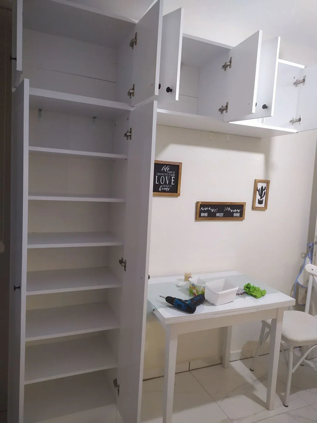 White kitchen with open cabinets revealing a small table and chairs.