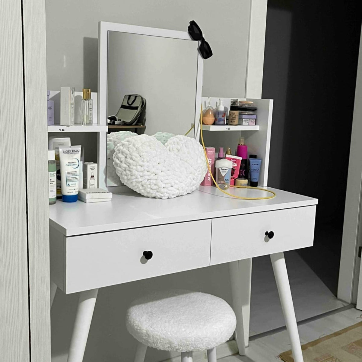 White vanity table with mirror, stool, and various items in a room.