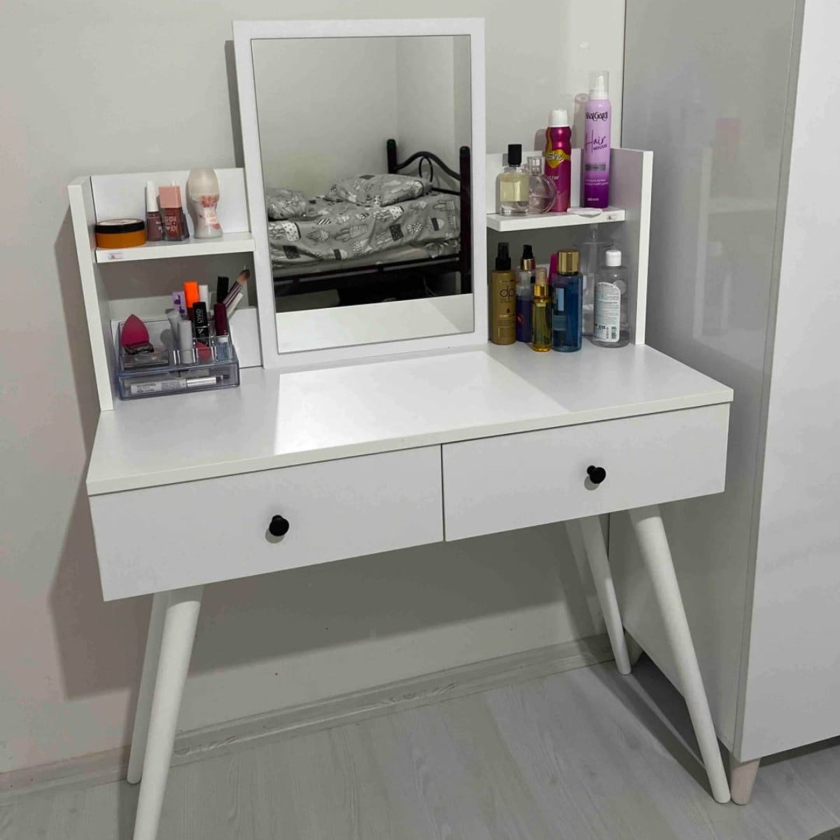 White vanity table with mirror and makeup items in a room.