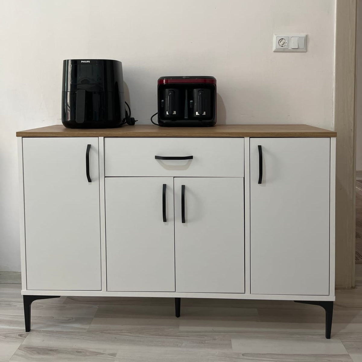 White cabinet with wooden top holding a coffee maker and toaster against a plain wall.