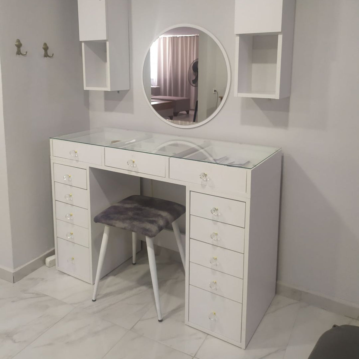 White vanity with round mirror and stool in a room.