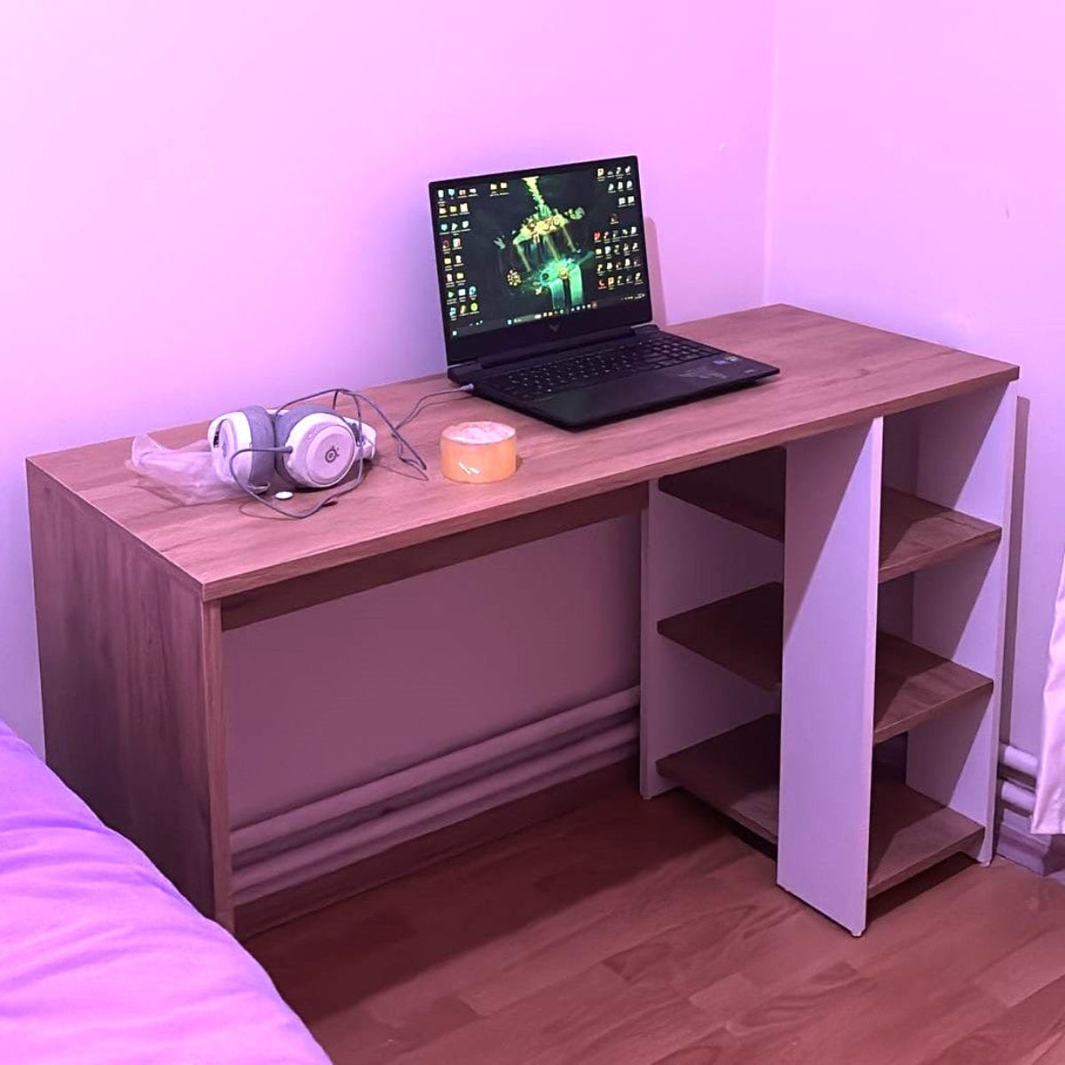 Wooden desk with a laptop, headphones, and a small container on a wooden floor.