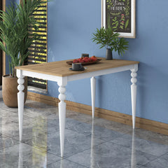 Wooden table with white legs against a blue wall with a plant and framed picture.