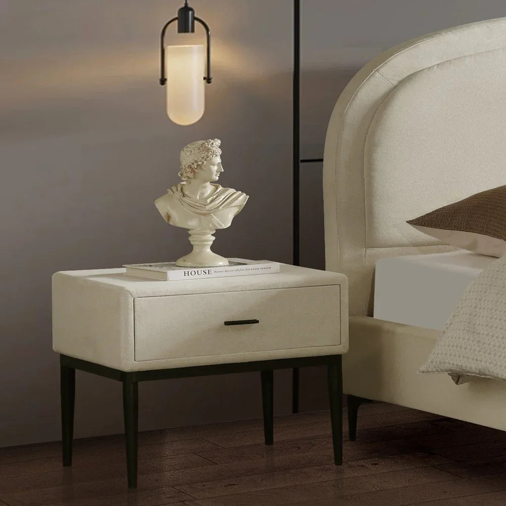 White nightstand with a bust and book next to a bed in a dimly lit room