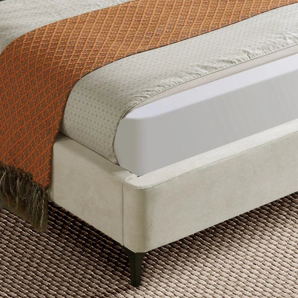 Close-up of a bed with a textured brown blanket and beige mattress on a carpeted floor.