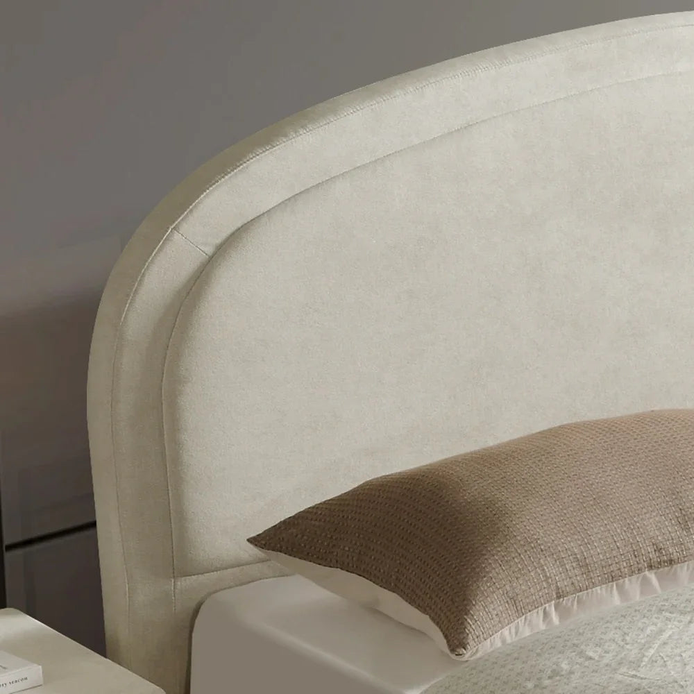 Close-up of a beige upholstered headboard with a brown pillow on a bed.