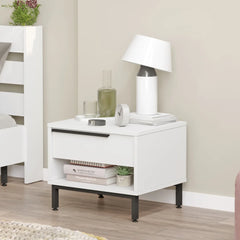 White nightstand with lamp and decor items next to a bed in a bedroom.