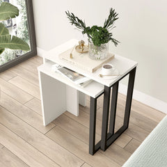 White side table with black legs on a wooden floor, featuring a plant and decorative items.