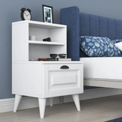 White nightstand with shelves next to a bed with blue headboard and pillows.