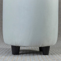 Close-up of a light gray upholstered chair with black legs on a textured surface.